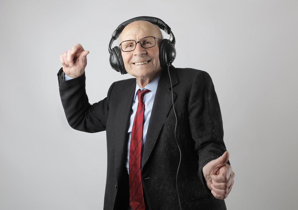 elderly white man with glasses in a suit is happily grooving to music piping through big headphones 